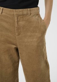 Bordeauxkleurige corduroy broek met verticale ribbels, voorzien van een standaard tailleband, zijzakken en een ontspannen pasvorm. Soepele structuur.