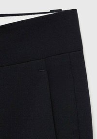 Pantalones negros ajustados con una textura suave, que presentan una cinturilla plana y un sutil patrón de espiga. Costuras laterales parcialmente visibles.
