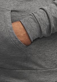 Main partiellement insérée dans la poche avant d'un sweat-shirt gris texturé à manches longues.