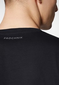 Czarny t-shirt z okrągłym dekoltem, o gładkiej fakturze i małym, szarym logo "PROCHNIK" na plecach. Prosty i minimalistyczny design.