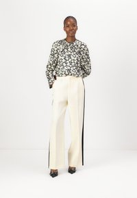 Blusa floreale con sfondo nero, maniche lunghe e scollatura plissettata abbinata a pantaloni a vita alta color crema con strisce laterali nere.