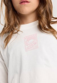 White long-sleeve t-shirt with a light pink graphic featuring "Malibu Beach" and a sun design, made from soft, textured cotton.