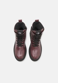 Burgundy lackläders ankle boots med svarta snören, rund tå och mjukt foder invändigt. Dragkedja på sidan för enkel påklädning.