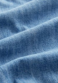 Tissu denim bleu clair doux avec une texture de tissage visible et des plis subtils créant de douces ombres.