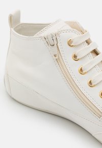 Baskets montantes blanches en cuir avec œillets dorés, détail de fermeture éclair texturé et lacets en coton plats. Fini lisse avec des accents minimes.