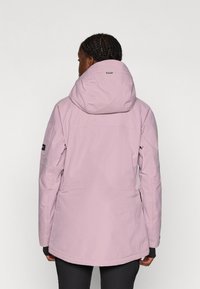 Világos rózsaszín vízálló dzseki, illeszkedő kapucnival, hosszú ujjakkal és kissé hosszabb hátrésszel. Az ujjon bal oldalon embléma található.