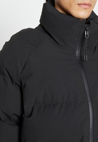 Schwarze Steppjacke mit hohem Kragen, ausgestattet mit einem Frontreißverschluss und gesteppten Paneeldetails, gefertigt aus glattem, wasserabweisendem Material.