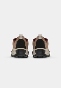 Vista traseira de sapatos de caminhada com uma combinação de camurça bege e detalhes pretos, possuindo uma sola de borracha texturizada e uma alça.