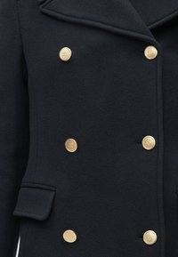 Marineblå uld-blandingsjakke med dobbeltbryst-design, gyldne knapper, klap krave og sidelommer for ekstra detalje.