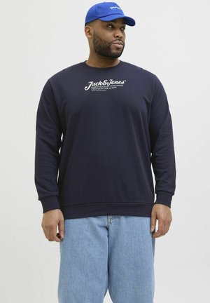Marineblaue Sweatjacke mit Rundhalsausschnitt und langen Ärmeln, versehen mit weißem, bedrucktem Logotext. Kombiniert mit hellblauen Jeans.