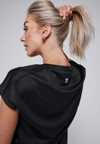 Zwart sportshirt met een ronde hals en korte mouwen, voorzien van een gestructureerde stof en een klein logo op de achterkant.