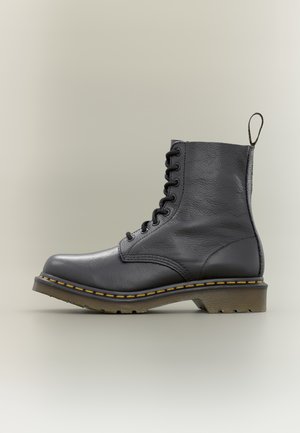 Bottine noire en cuir à lacets avec surpiqûres jaunes, semelle épaisse marron, et languette de tirage à l'arrière, vue de côté.