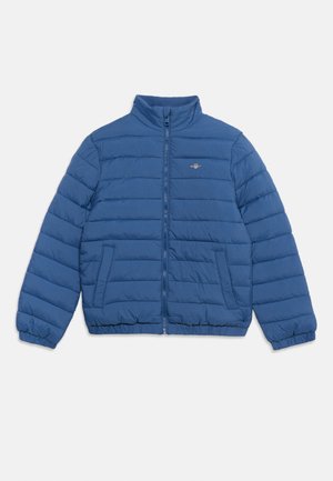 Giacca imbottita trapuntata blu con cerniera frontale completa, collo alto, polsini elastici, due tasche frontali e piccolo logo sul petto sinistro.