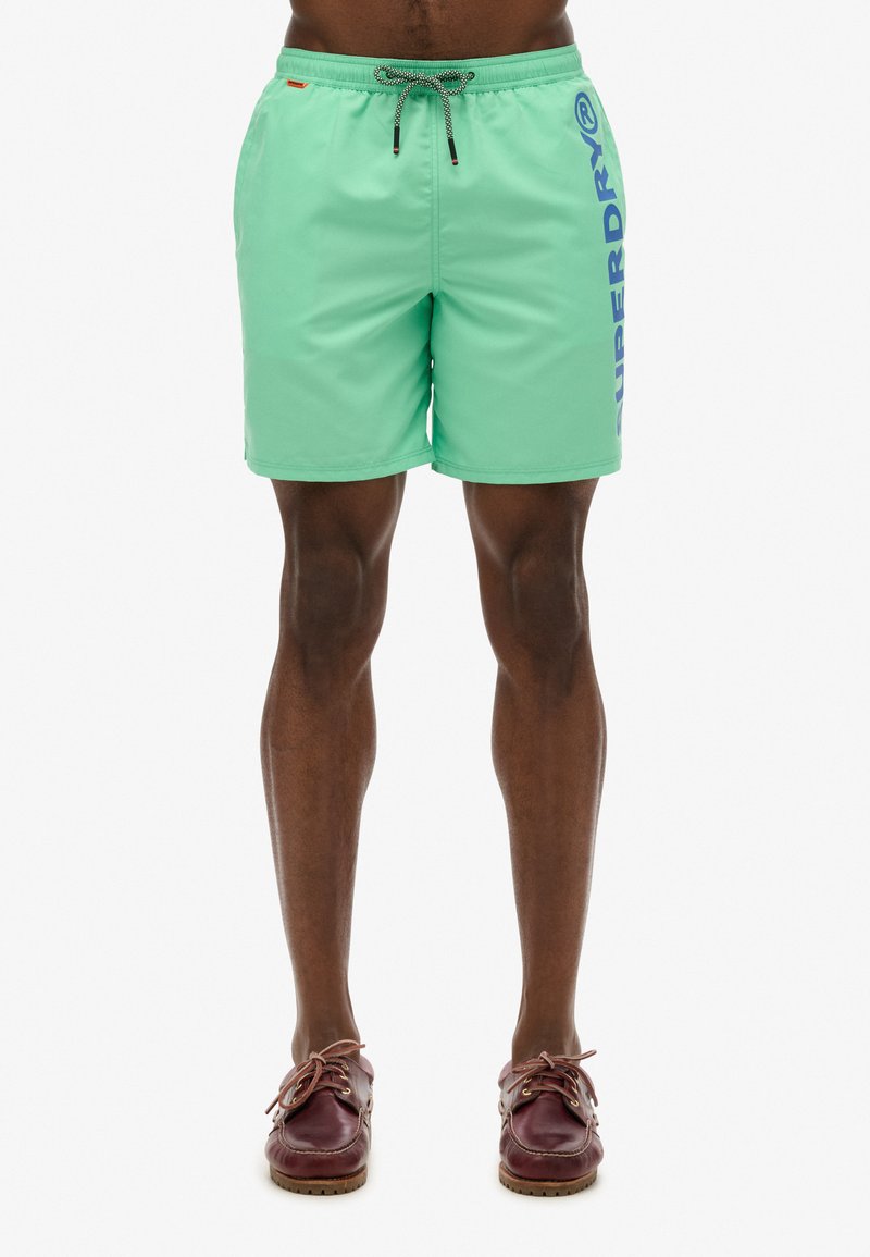 Shorts da bagno verde menta con vita elastica e coulisse, caratterizzati da un grande logo blu "SUPERDRY" sul lato. Texture liscia.
