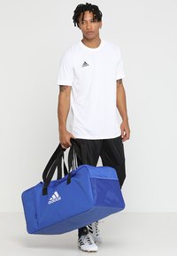 Borsa a borsa blu realizzata in tessuto resistente, con manici neri e logo Adidas bianco. Il design include un ampio scomparto principale e dettagli in rete.