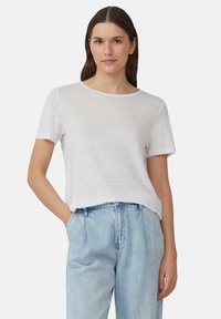 T-shirt blanc à manches courtes avec une coupe décontractée et un col arrondi, fabriqué à partir d'un tissu léger et texturé. Porte avec un jean taille haute bleu.