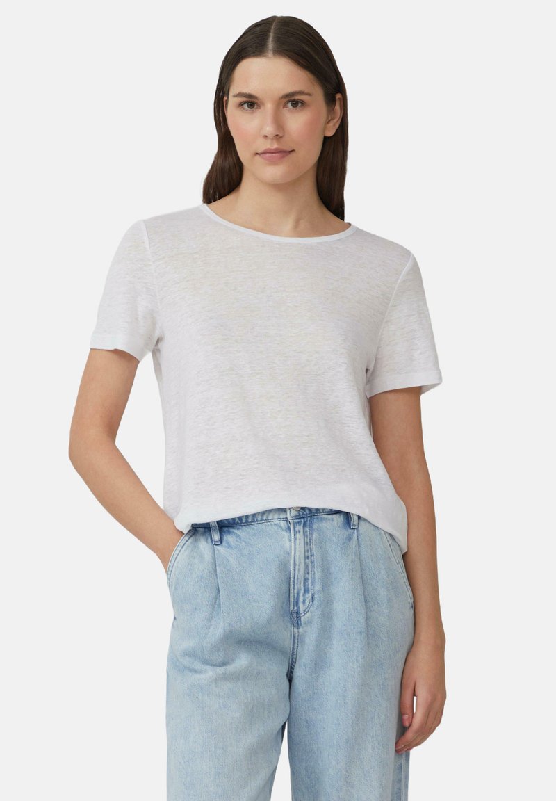 T-shirt blanc à manches courtes avec une coupe décontractée et un col arrondi, fabriqué à partir d'un tissu léger et texturé. Porte avec un jean taille haute bleu.
