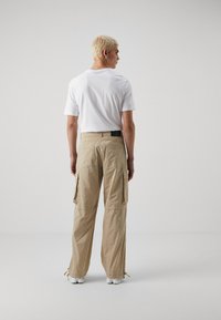 Kaki cargo bukser med løs pasform, med sidelommer og justerbare nederste kanter, parret med en ensfarvet hvid T-shirt.