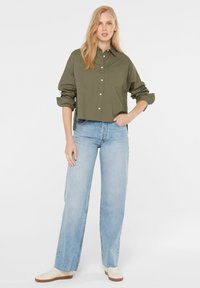 Olive green cropped button-up shirt with long sleeves, paired with light blue wide-leg jeans and white sneakers with brown soles.