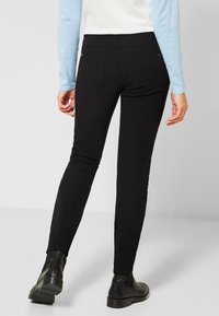 Svarta smala jeans med en slät textur, försedda med bakfickor och en midjehöjd på mellanläge, ihop med svarta ankelstövlar.