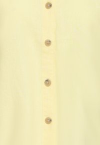 Gros plan sur quatre boutons marron sur un tissu jaune clair, disposés verticalement le long d'une couture.