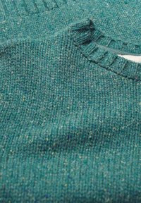 Pleteni pulover u tirkiznoj boji s višečlanim točkicama. Ima rebrasti okrugli izrez i teksturirani materijal, što daje ugodan izgled.