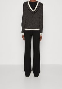 Sweat à capuche noir avec une texture scintillante, bord crème contrastant. Associé à un pantalon noir à jambes larges avec un poignet marqué.