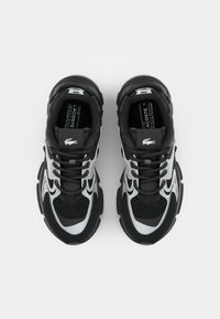 Zapatillas deportivas en negro y gris con parte superior de malla, lengüeta acolchada y suela de goma texturizada; cuenta con detalles del logo y diseño con cordones.