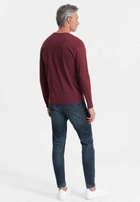 Bordeauxkleurig overhemd met lange mouwen en een ronde halslijn, gecombineerd met donkerblauwe slim-fit jeans en witte sneakers; eenvoudig ontwerp, geen zichtbare patronen.