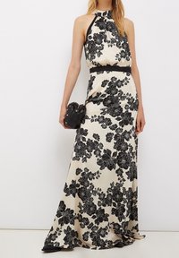 Sukienka maxi w kwiaty z dekoltem halter, czarnym wzorem florystycznym na kremowym tle i czarnym paskiem w talii. Gładka tekstura materiału.