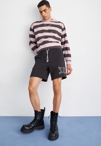 Pantalones cortos negros con bordado de calavera y tibias cruzadas, combinados con una camiseta de manga larga a rayas rosas y negras y botas de combate negras.