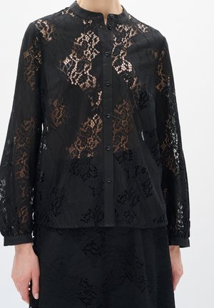 Blusa negra de encaje de manga larga con estampado floral, botones en la parte delantera y escote sin cuello, combinada con falda de encaje a juego.