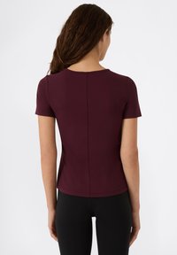 Top burdeos de manga corta con un diseño ajustado, textura de canalé, cuello redondo y costura central en la parte trasera, combinado con leggings negros.