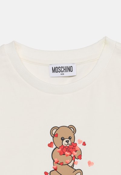 T-shirt blanc pour enfant avec label de la marque Moschino et graphisme d'ours en peluche tenant des cœurs rouges sur le devant.