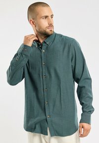 Grüne Hemdbluse aus strukturiertem Stoff, mit Kragen, langen Ärmeln und braunen Knöpfen entlang der Vorderseite.