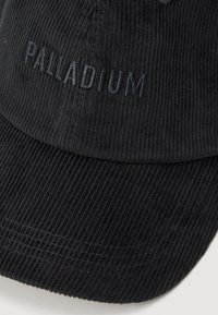Čierna kordurová baseballová čiapka s zakriveným šiltom a vyšitým nápisom "PALLADIUM" čiernou niťou na prednom panely.