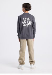 Gray sweatshirt with a white graphic design on the back; paired with light beige pants and white sneakers. Soft fabric with a relaxed fit.
