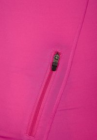 Tajtat rosa tyg med en liten svart dragkedjeficka och slät textur; sömdetaljerna är subtila och välintegrerade.