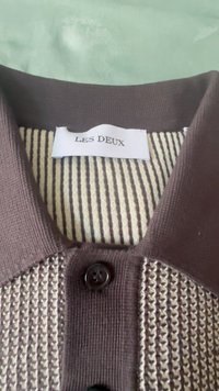 Brun cardigan med ett texturerat, stickat mönster och en randig beige insida. Har en svart knapp och varumärkesetikett "LES DEUX" på kragen.