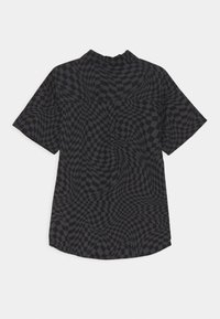 Košile s krátkým rukávem, deformovaným černým a tmavě šedým kostkovaným vzorem a vysokým límečkem, zobrazená zezadu na jednobarevném pozadí.