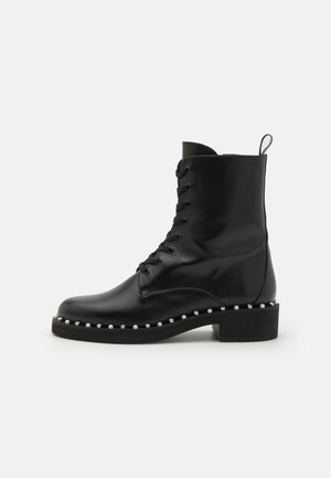 Bottine noire en cuir avec fermeture à lacets, bout rond, semelle plate et décorations en clous sur le périmètre de la semelle.