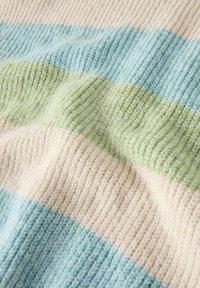 Paski dzianinowy koc w miękkich pastelowych kolorach: jasnoniebieski, jasnozielony i beżowy. Gruba tekstura z prążkowanym wzorem i lekkim meszkiem.