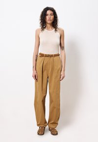 Beige geribbelde tanktop gecombineerd met tan hoge cargobroek met grote zakken en een gevlochten riem. Draagt een paar bruin gespen sandalen.