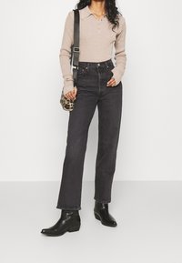 Jeans de tiro alto oscuros combinados con una camiseta de polo de manga larga de color marrón claro y botas negras de tobillo. Un pequeño bolso de estampado de leopardo está colgado del hombro.