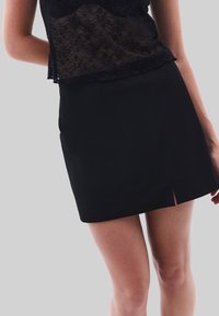 Svart minikjol med rak silhuett, pryd med en framklippa för detaljer, tillverkad av ett mjukt tyg. Idealisk för olika avslappnade stilar.