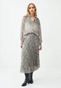 Panterprint, doorschijnende blouse en geplooide maxi-rok in neutrale tinten, gecombineerd met zwarte kniehoge laarzen. Bevat een V-hals en elastische manchetten.