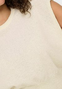 creMEfarbener, gestrickter Pullover mit strukturiertem Oberflächen, weitem Rundhalsausschnitt und ärmellosem Design. Zeigt einen weichen, leichten Stoff.
