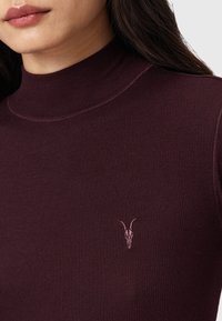 Burgunderfarbener, gerippter Rollkragenpullover mit glatter Textur, der auf der Brust ein dezent gesticktes Ziegenschädel-Detail aufweist.