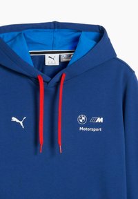 Blauer Hoodie mit roten Kordeln, versehen mit einem weißen Puma-Logo und BMW Motorsport-Branding. Das Material wirkt weich; mit blauem Stoff gefüttert.