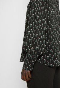 Blouse noire en tissu léger, ornée d'un motif abstrait multicolore et de manches longues froncées avec des poignets boutonnés.